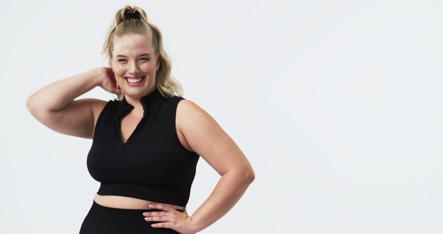 Caucasian beautiful plus size woman posing confidently in studio, smiling with hand on hip, copy space. Bright white background emphasizes her joyful expression and body positivity, unaltered