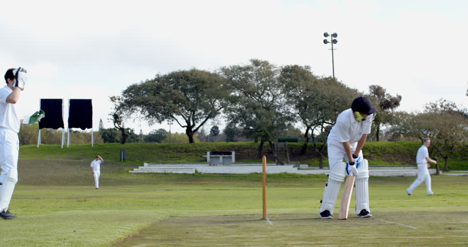 Two teams of multiracial male cricket players and male umpire playing cricket on pitch. sports, activity, teamwork, competition and cricket.