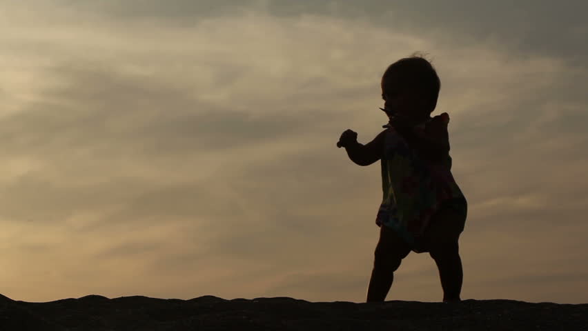 Outline of small girl walking over sunset
