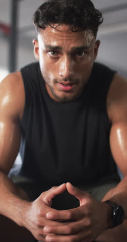 Vertical video: Resting after intense workout, sweaty man sitting and catching breath in gym. Fitness, exercise, training, resilience, endurance, sports