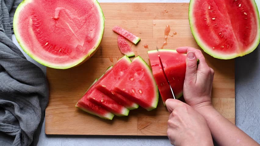 Female hands cutting fresh juicy watermelon slices on cutting board.