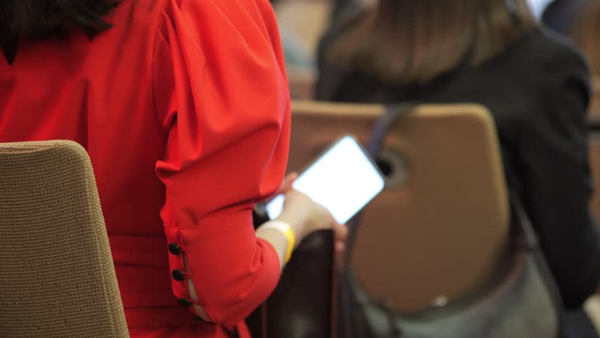 Woman in a red shirt is looking at her phone. She is sitting in a chair with her back to the camera