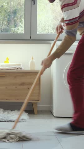 Man cleaning a water leak on the bathroom floor using a mop, the sink is leaking