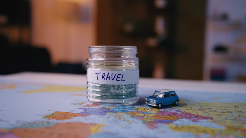 Woman's hand places dollars into a glass jar, saving money for a future trip