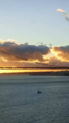 View of 25 de Abril Bridge famous tourist landmark of Lisbon connecting Lisboa and Almada on Setubal Peninsula over Tagus river on sunset. Lisbon, Portugal. Camera pan