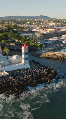 Aerial view of Santa Marta lighthouse and Cascais marina with moored yacht boats with Cascais cityscape, Portugal on sunset. Orbit parallax shot