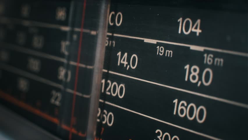 Close-up of a radio dial as the needle moves across frequencies. The red indicator highlights different stations on the old-fashioned receiver.