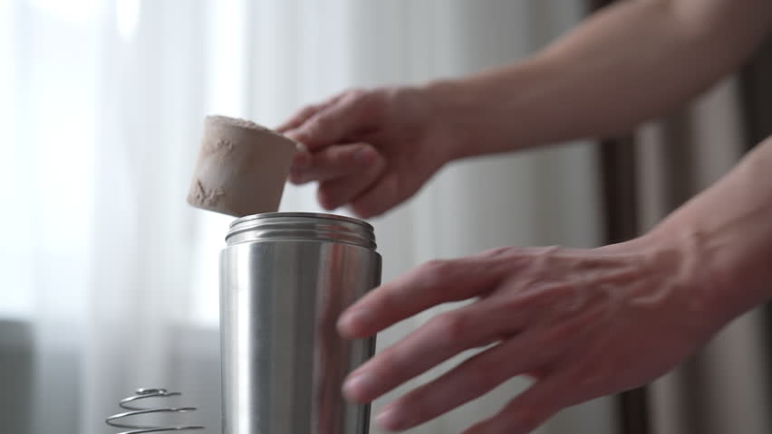 Close-up hand of unrecognizable bodybuilder pouring protein powder into metal shaker bottle, preparing post-workout recovery drink or meal replacement shake. Concept importance of sports nutrition.