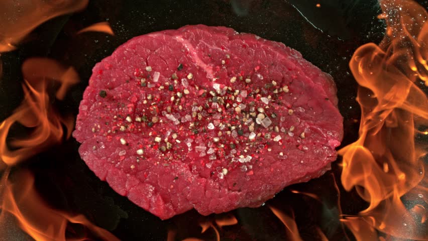 Super Slow Motion Shot of Raw Beef Steak Throwed into Fired up Pan with Flames at 1000fps.