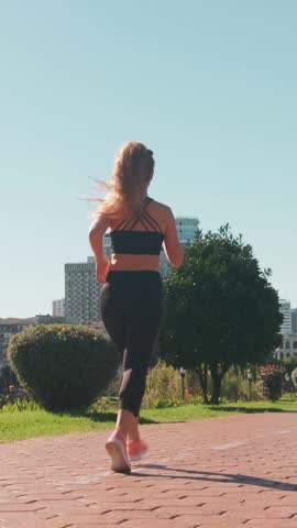 Manager does morning run before start of working day. Woman in black tracksuit runs on treadmill against backdrop of giant modern buildings of city.
