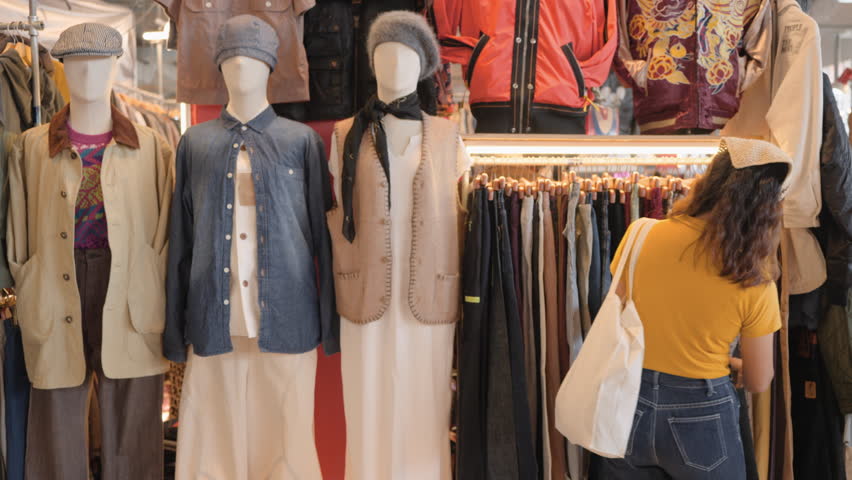 Young teen tourist Gen Z asia female choose look at zero waste eco go green buy second hand sale store flea market thrift old used vintage fabric style. Happy woman city asian people small retail shop