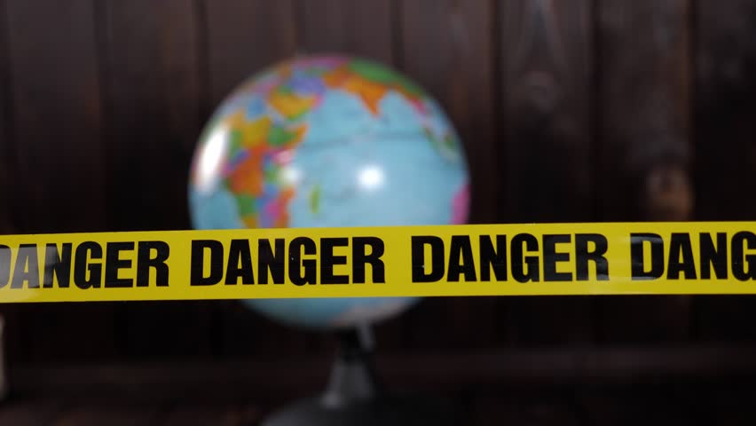 Close-up of a globe on a dark wooden background, in the foreground a yellow warning tape with the inscription DANGER. World problems. Ecology and protection of the planet.