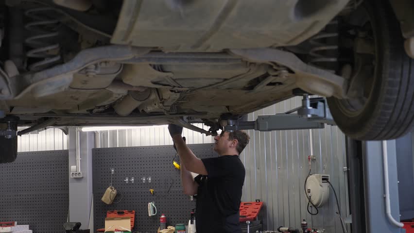 An auto mechanic working under a car on a car lift in a garage. Auto repair shop, auto repair. Repair of the bottom of the car in a modern auto repair shop.