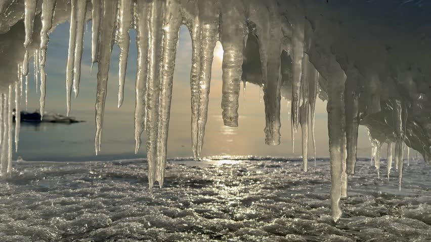 Video of Baikal Lake on January morning. Ice arch with icicles on the icy beach during freeze-up on the lake. Beautiful winter sunrise landscape. Changing seasons, natural phenomena 