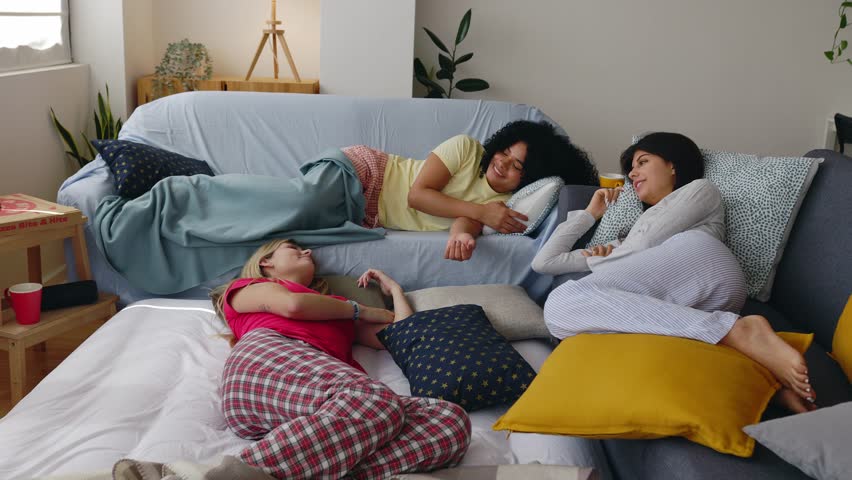 Three young teenage girls hanging out relaxing on sofas after slumber party at home. Female friendship and youth community concept
