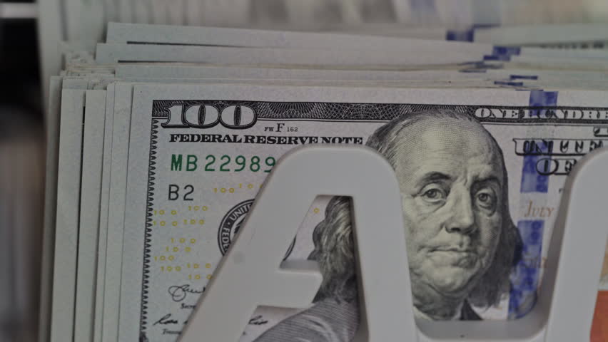 A detailed view of neatly stacked hundred dollar bills with a prominent display stand visible. The cash arrangement showcases its value in a retail setting.