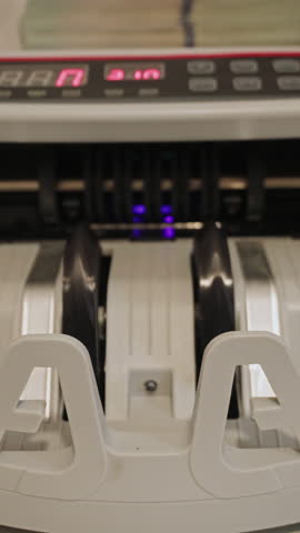 A cash counting machine processes a stack of dollar bills, showcasing images of money and revealing the efficiency of transactions in a financial setting. Vertical video.