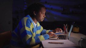 Young African American woman tired an bored taking notes in notebook and using laptop at home working late. Female university student studying at night in the living room. Video with copy space. - Powered by Shutterstock - Get 15% off with code: PIKWIZARD15