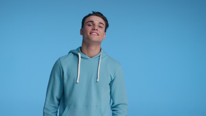 confident casual man wearing blue hoodie smiling while standing with arms folded on blue background