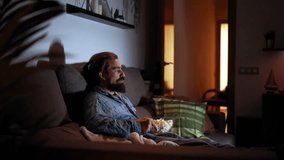 Side view footage of a man sitting on the sofa at home watching movies and eating popcorns. Copy space video. - Powered by Shutterstock - Get 15% off with code: PIKWIZARD15