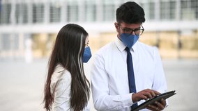 Professional business partners wearing protective face masks collaborating while using digital tablet in front of modern office building, representing safe workplace interaction during pandemic era - Powered by Shutterstock - Get 15% off with code: PIKWIZARD15