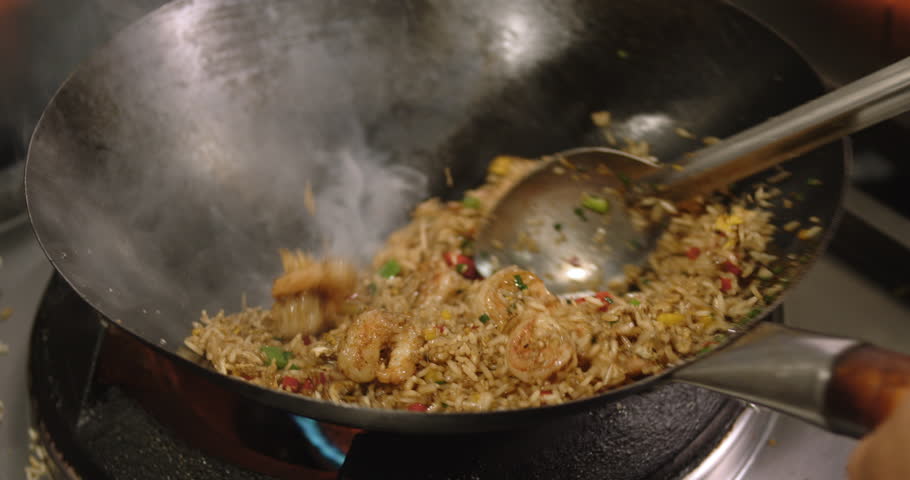 A closeup footage of a chef frying the Peruvian Chaufa Rice with Seafood (Arroz Chaufa con Mariscos) in a wok on a gas stove, with blurred background