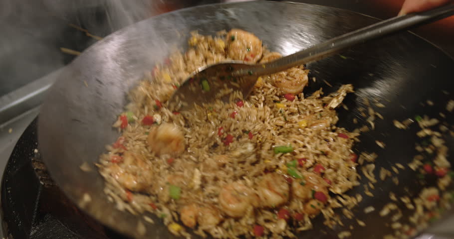 A closeup footage of a chef frying the Peruvian Chaufa Rice with Seafood (Arroz Chaufa con Mariscos) in a wok on a gas stove, with blurred background