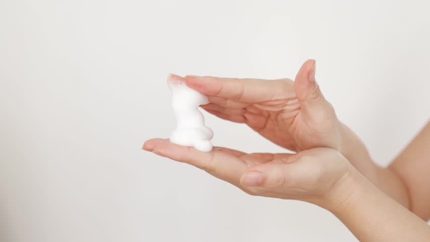 Extreme close up, hands on isolated background, young woman applying hand foam soap or foam to wash face, skin care, cleansing, hygiene, health care. Finger presses taking foam from bottle Slow motion