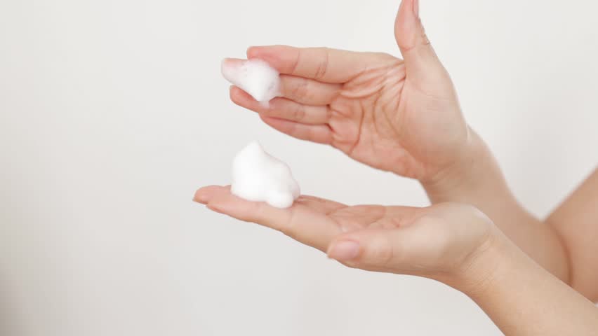 Extreme close up, hands on isolated background, young woman applying hand foam soap or foam to wash face, skin care, cleansing, hygiene, health care. Finger presses taking foam from bottle Slow motion