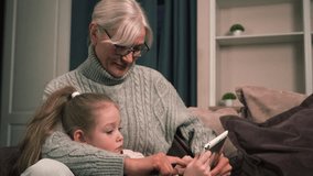 Grandmother and granddaughter focus on solving fun interactive puzzles on a tablet, sitting together on the couch at home. - Powered by Shutterstock - Get 15% off with code: PIKWIZARD15