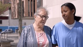 Senior caucasian woman outside retirement home with a female nurse. Footage of a young latina caregiver out for a walk outdoors with her female senior patient. - Powered by Shutterstock - Get 15% off with code: PIKWIZARD15