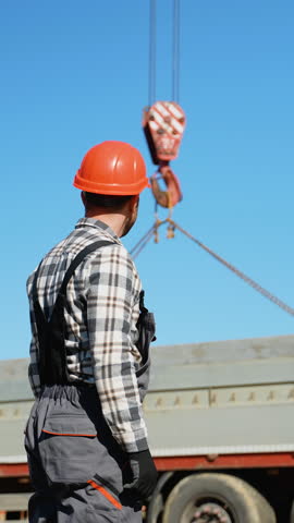 A foreman in a hard hat signals to a crane operator while lifting a concrete slab at a busy construction site