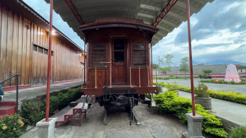 Visitors enjoy a close-up view of an old train at the museum in Granada, Nicaragua, surrounded by lush greenery and historic architecture under a cloudy sky.