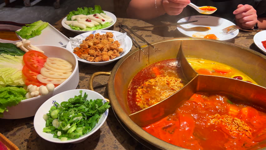 Eating a traditional Chinese Hot Pot with three brothes, noodles, tteokbokki, beef, fried chicken and vegetables, hot pot with steam at a restaurant, authentic taste experience, 4K shot