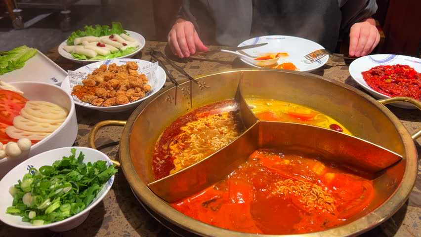 Eating a traditional Chinese Hot Pot with three brothes, noodles, tteokbokki, beef, fried chicken and vegetables, hot pot with steam at a restaurant, authentic taste experience, 4K shot