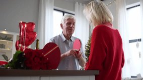 loving elderly couple of seniors celebrate Valentine's day at home, old man gives valentine card and congratulates his wife with flowers and wine, pensioners on romantic date - Powered by Shutterstock - Get 15% off with code: PIKWIZARD15