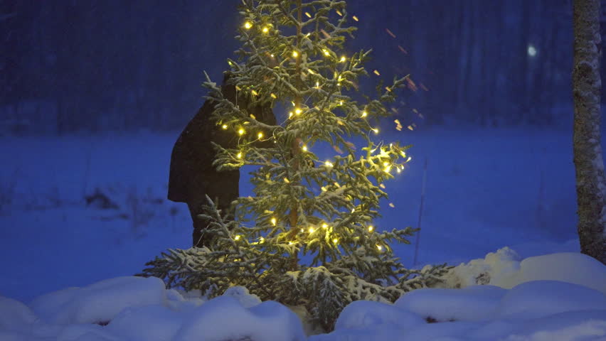 Woman decorating Christmas tree at dusk in his snowy garden