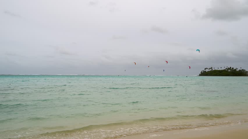 Kitesurfers on a grey, windy and cloudy day at Tropical Beach on Rarotonga, Cook Islands.