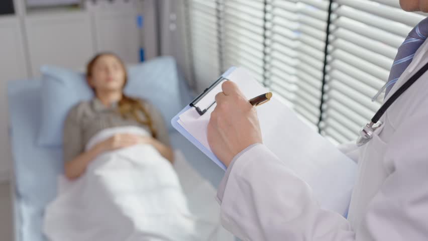 Close up of doctor examine patient woman lying on bed in recovery room. Professional mature medic working to support, give diagnosis treatment to young sick girl in health care clinic at hospital ward