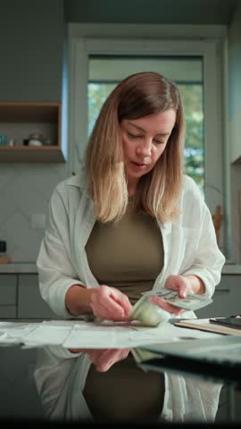 Woman calculating domestic bills and counting remaining money, sitting at kitchen table and planning personal finance. Concept of rising costs in households