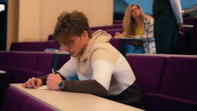 Montage showcasing a focused male student diligently taking notes during a university lecture, captured in slow motion, with other students and a professor in the background - Powered by Shutterstock - Get 15% off with code: PIKWIZARD15