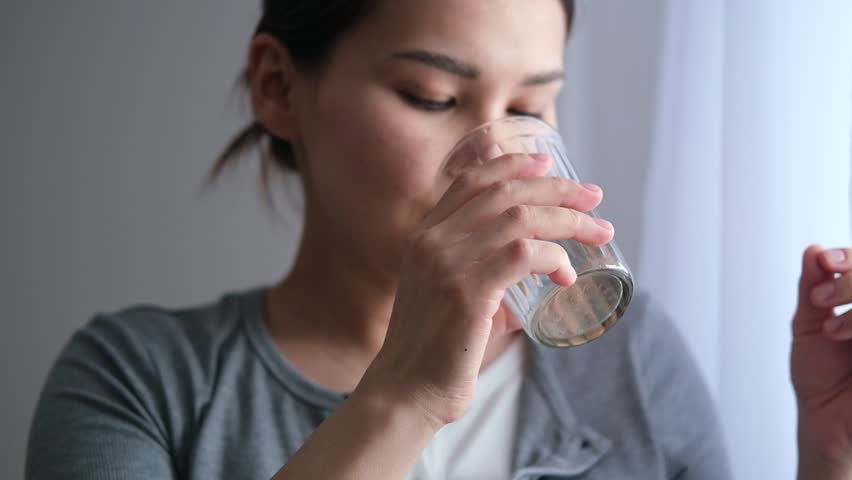 Asian pregnant woman is taking pills and vitamins for pregnant women with capsule on her hand and water. Drinking a tablet with a glass of water