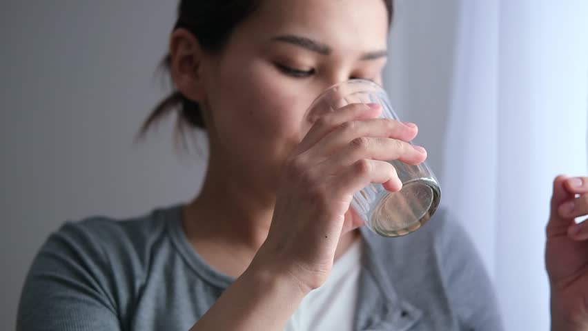Asian pregnant woman is taking pills and vitamins for pregnant women with capsule on her hand and water. Drinking a tablet with a glass of water