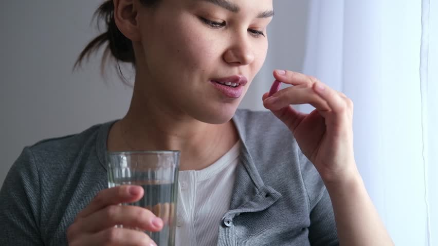 Asian pregnant woman is taking pills and vitamins for pregnant women with capsule on her hand and water. Drinking a tablet with a glass of water