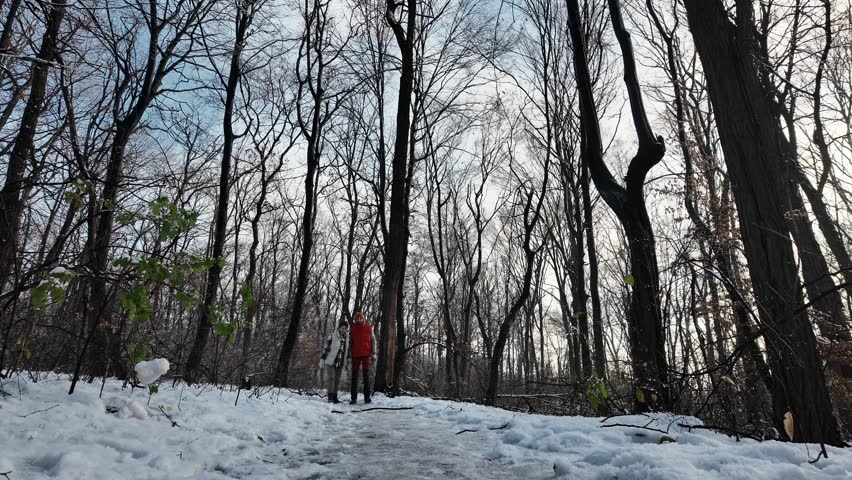 A young Caucasian couple walking together in a snowy park on a sunny winter day. Woman and man walk outside, walking along the snowy paths together. Front view