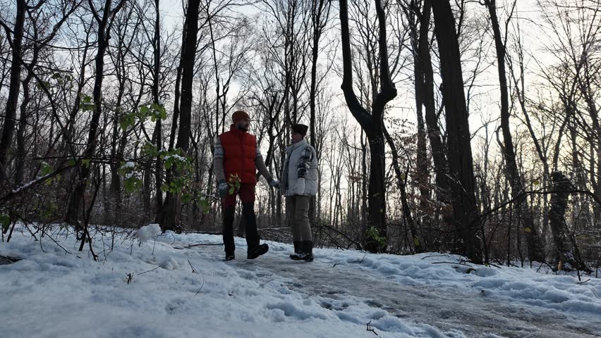 A young couple walking together in a snowy park on a sunny winter day. Woman and man walk outside, walking along the snowy paths in forest together. A happy couple dancing and hugging during a hike