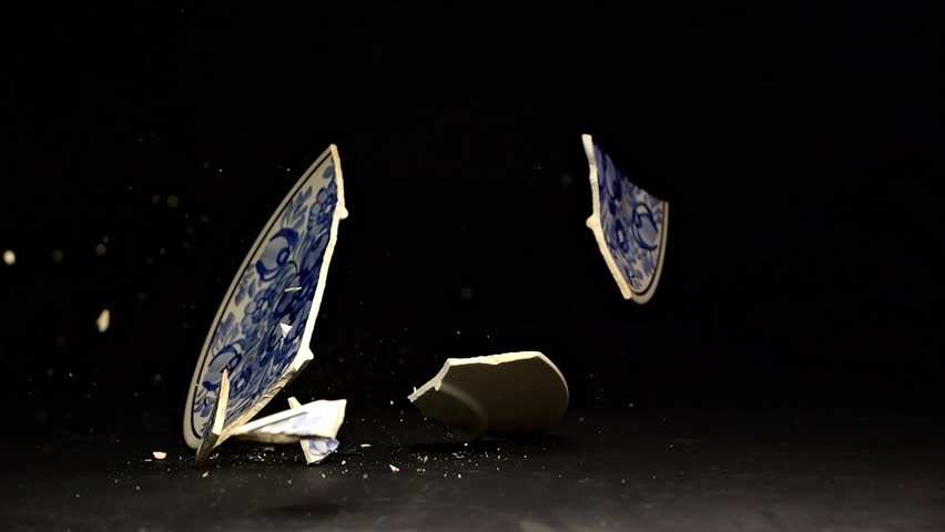 Slow-motion footage of a hand-painted plate breaking on impact with the floor. Shards fly outward, set against a sleek matte black surface.
