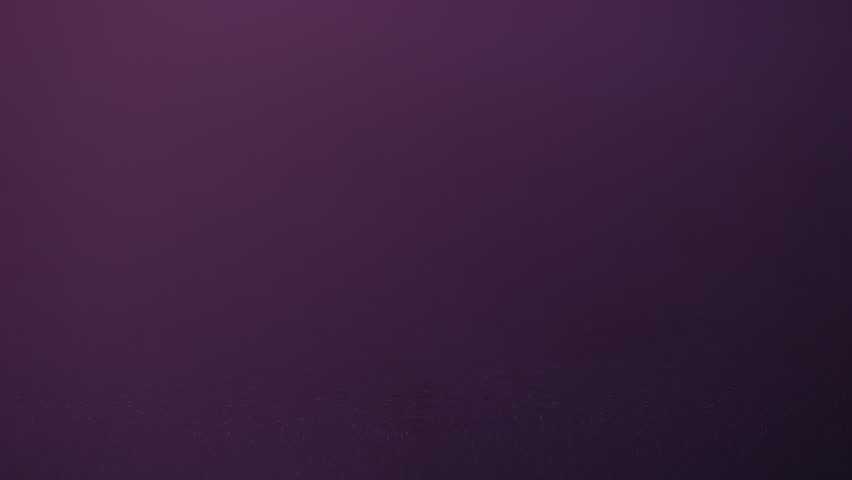 A drop lands on a smooth pink-purple water surface, producing a crown splash and spreading concentric ripples in slow motion.