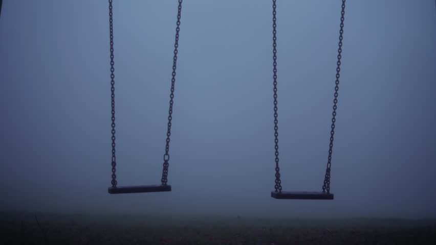 Children swings in eerie dark foggy playground medium 4k shot selective focus