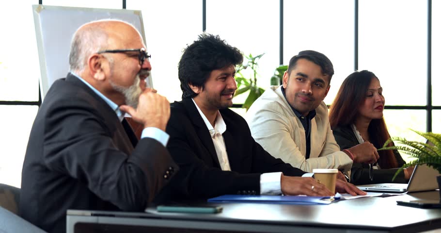 Indian Asian group of four successful business professionals in executive attire, sitting at one side of the conference table, discussing or interviewing someone